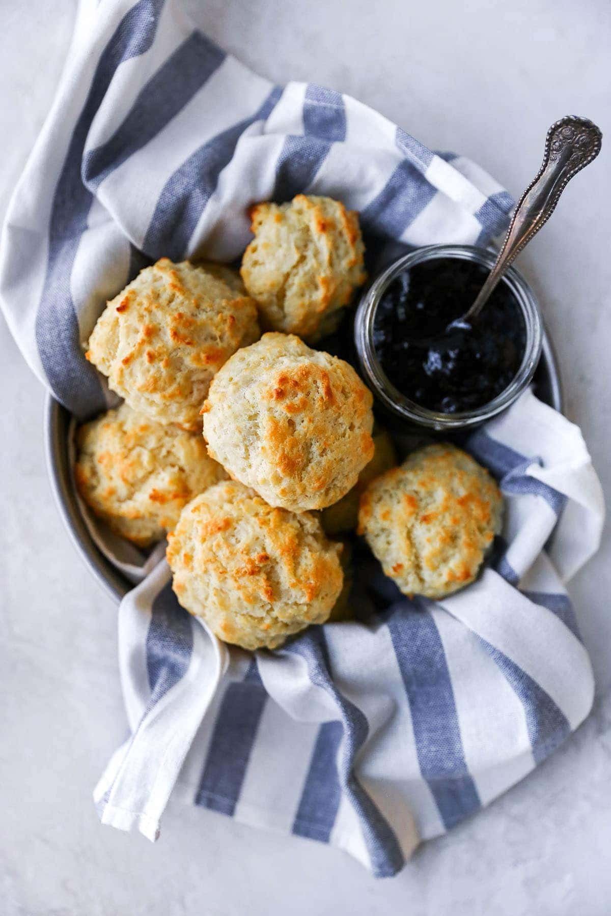 Buttermilk Drop Biscuits in bowl with towel and jar of jam. 