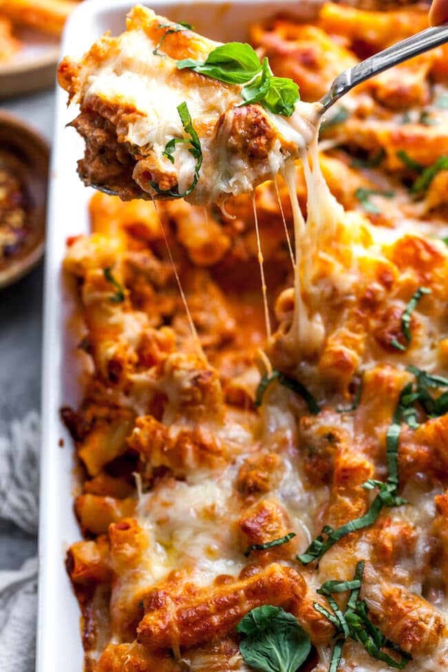 Baked ziti on a serving spoon being served from a baking dish. 