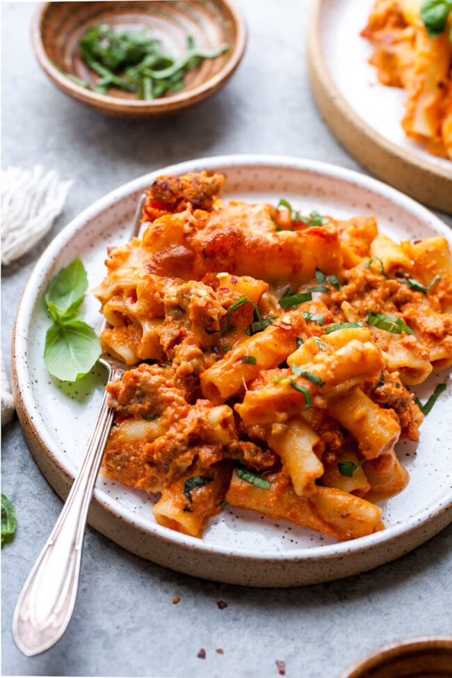 baked ziti with sausage and fresh basil on plate with fork. 