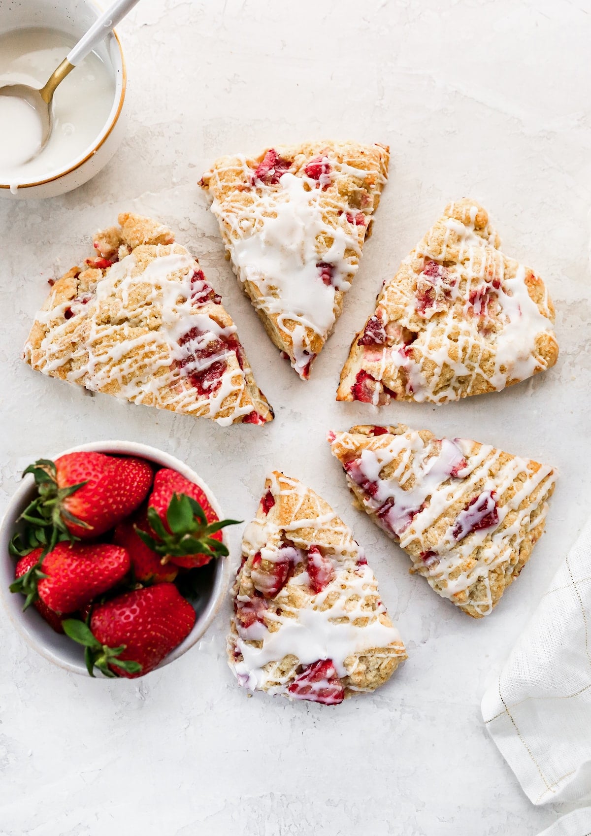 glazed strawberry scones with a bowl of fresh strawberries.