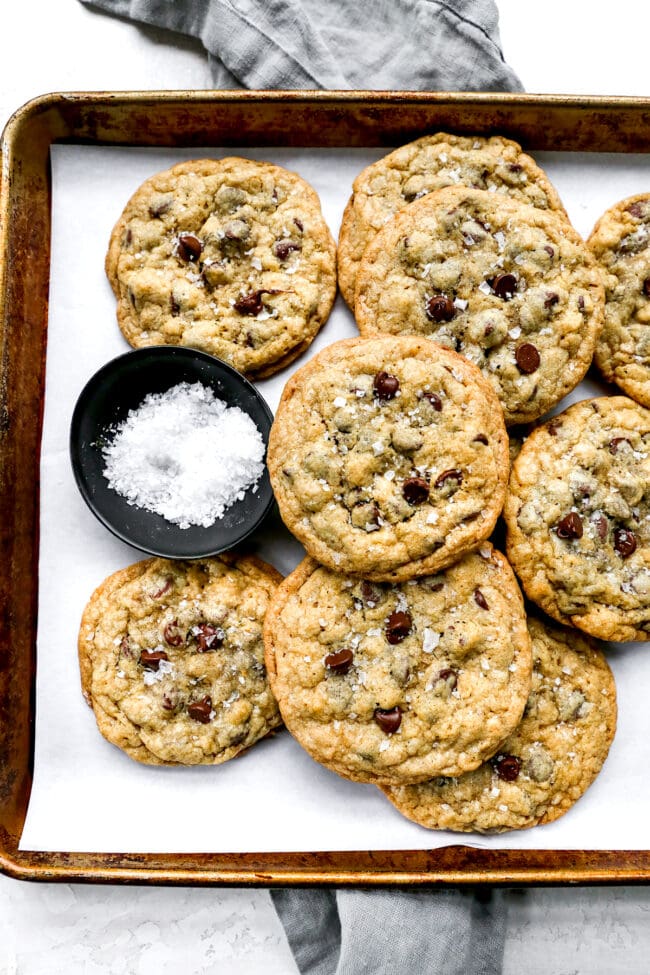 Doubletree Cookies on baking sheet with parchment paper and small bowl of flaky sea salt. 