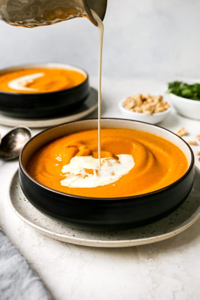 Carrot Ginger Soup in bowl with coconut milk being poured on top