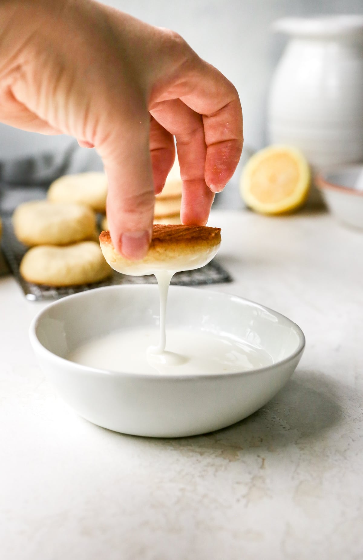 lemon cookies being dipped in a bowl of lemon glaze.