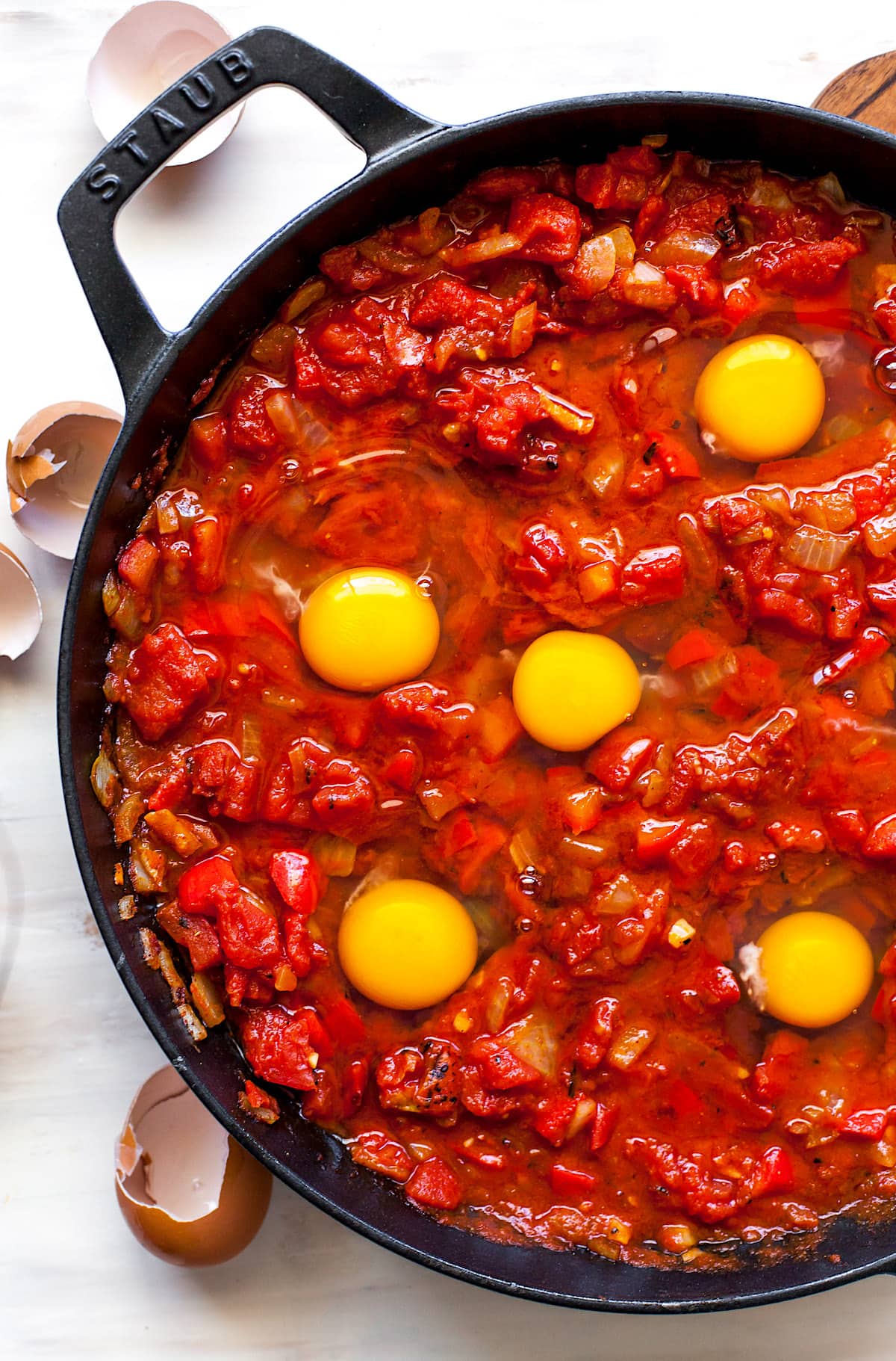 cracked eggs in tomato sauce in skillet to make shakshuka. 