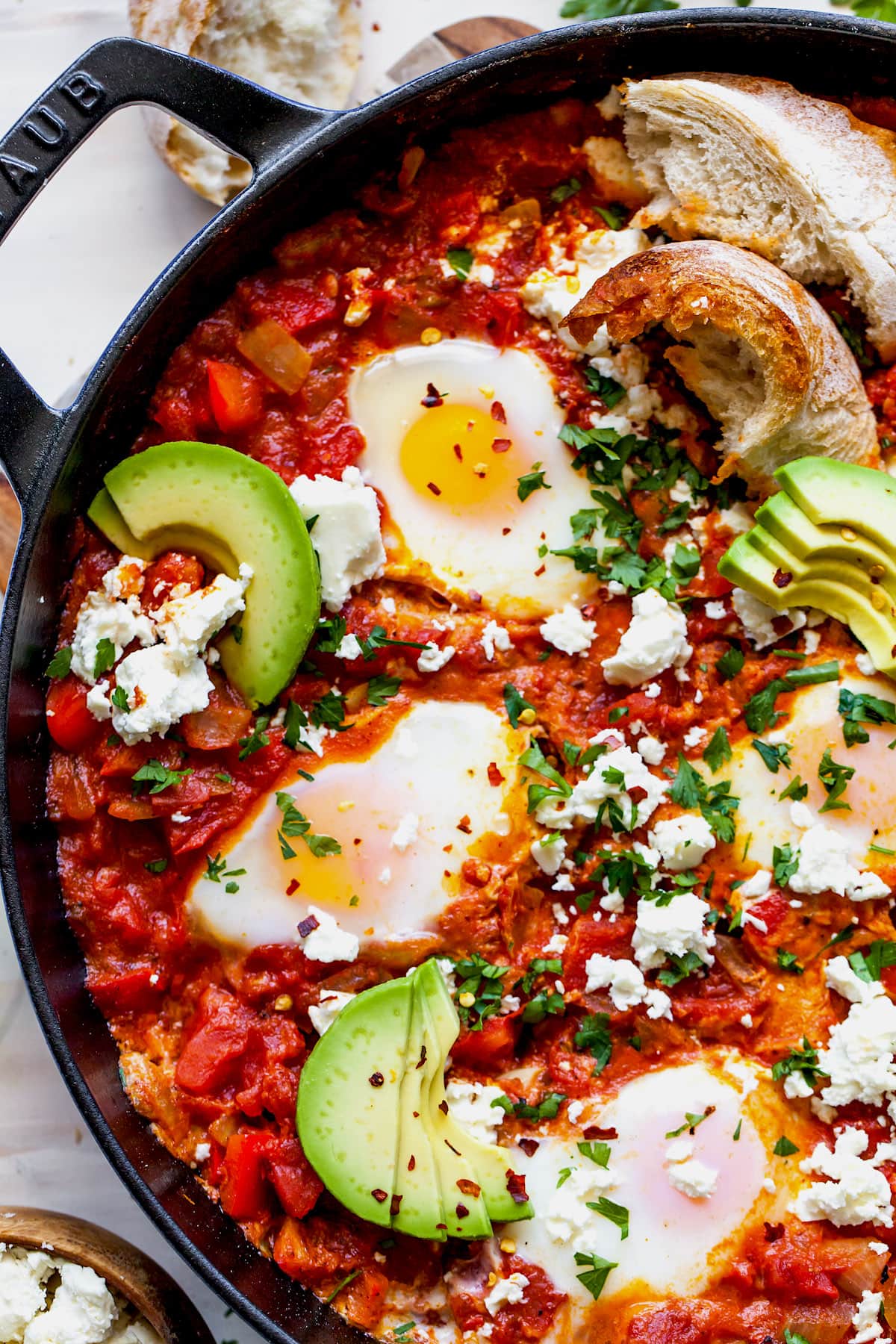 Shakshuka Eggs in skillet with feta cheese, herbs, and avocado slices. 
