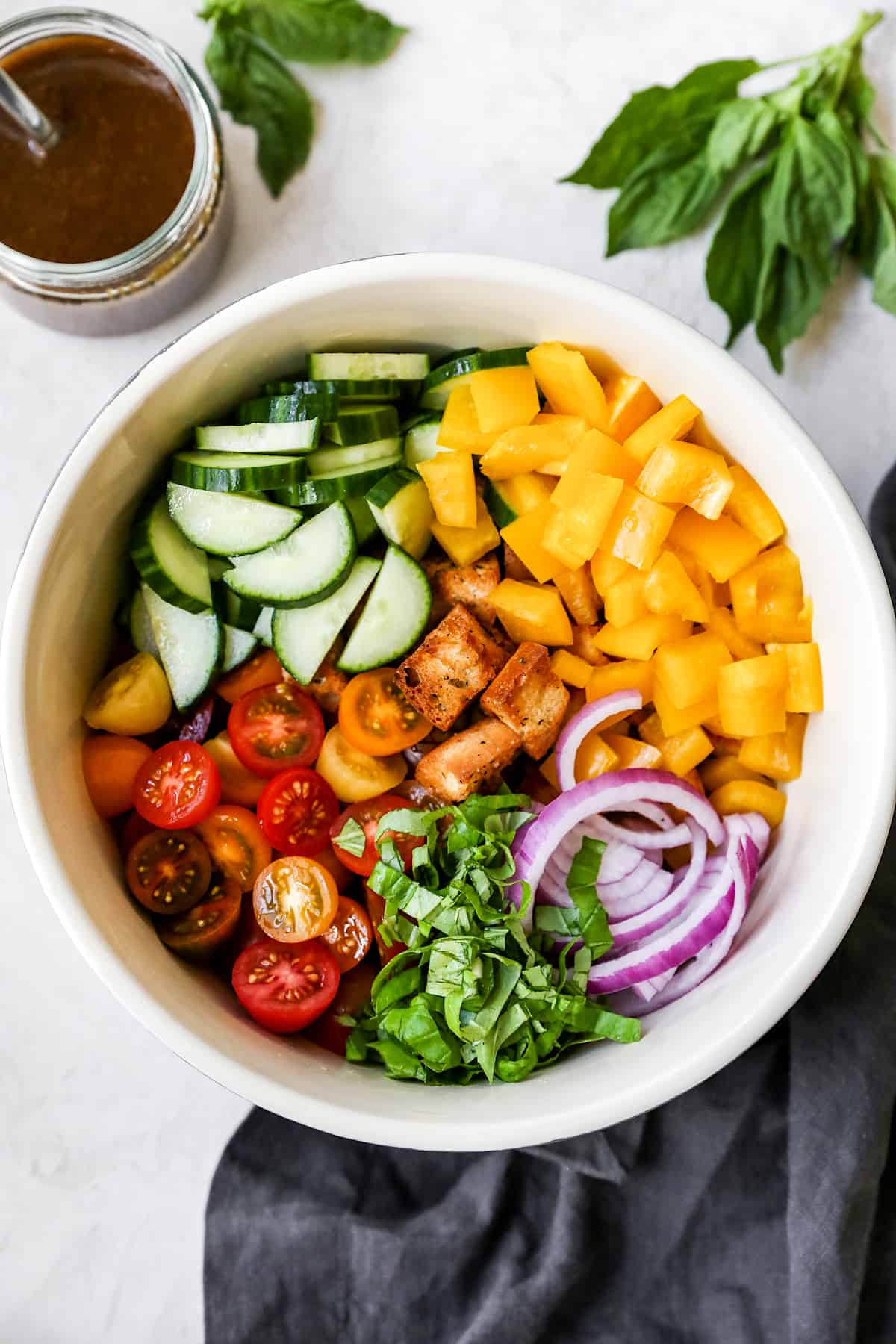 cucumber, peppers, red onion, basil, tomatoes, and homemade croutons in bowl to make panzanella. 