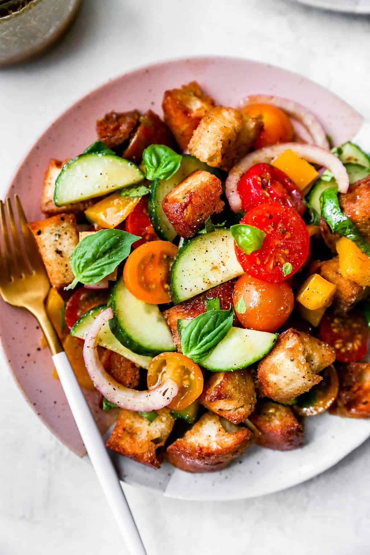 Panzanella salad in bowl with tomatoes, cucumber, peppers, onion, and fresh basil. 