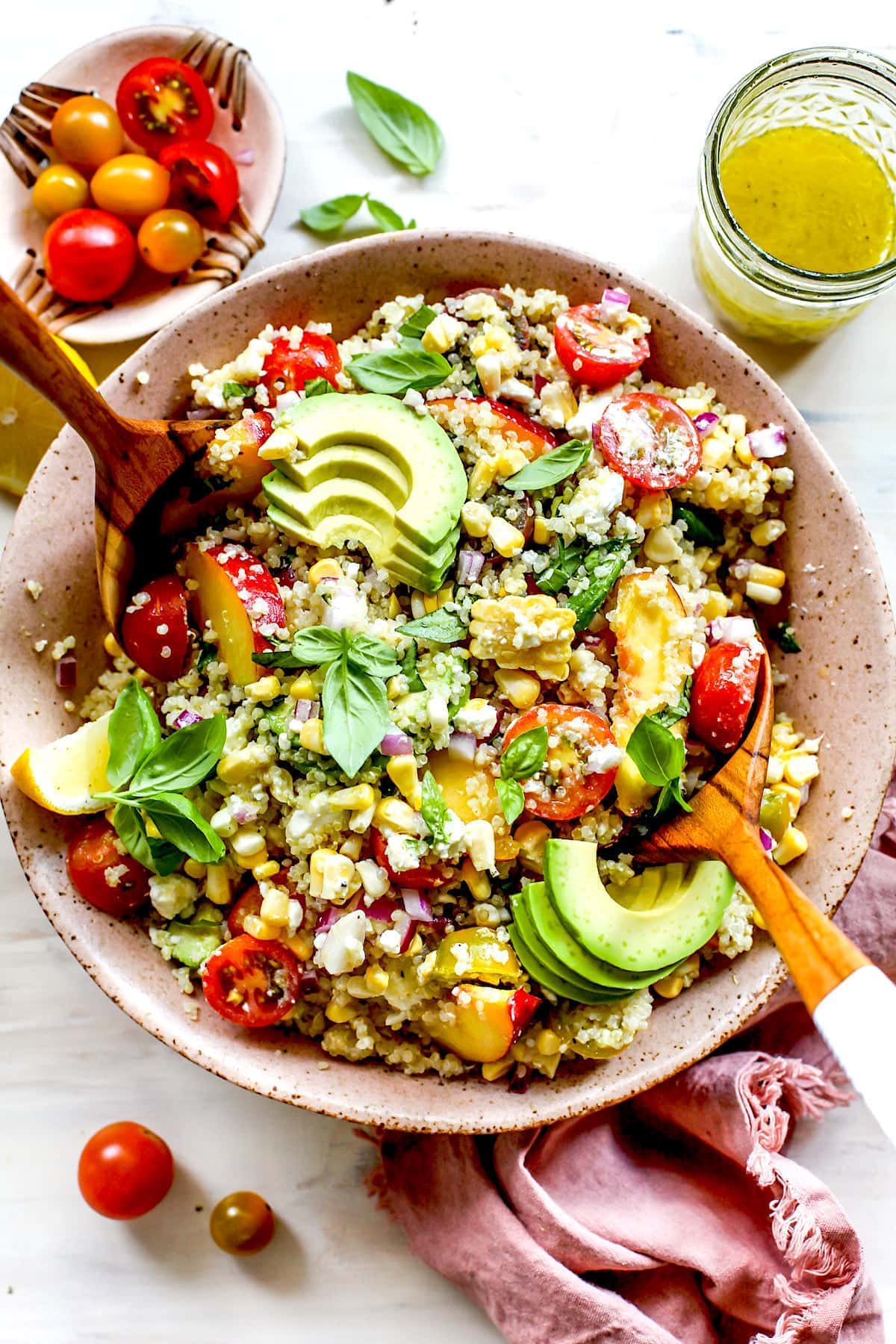 Summer Quinoa Salad in bowl with basil, avocado, tomatoes, corn, and wood salad servers.