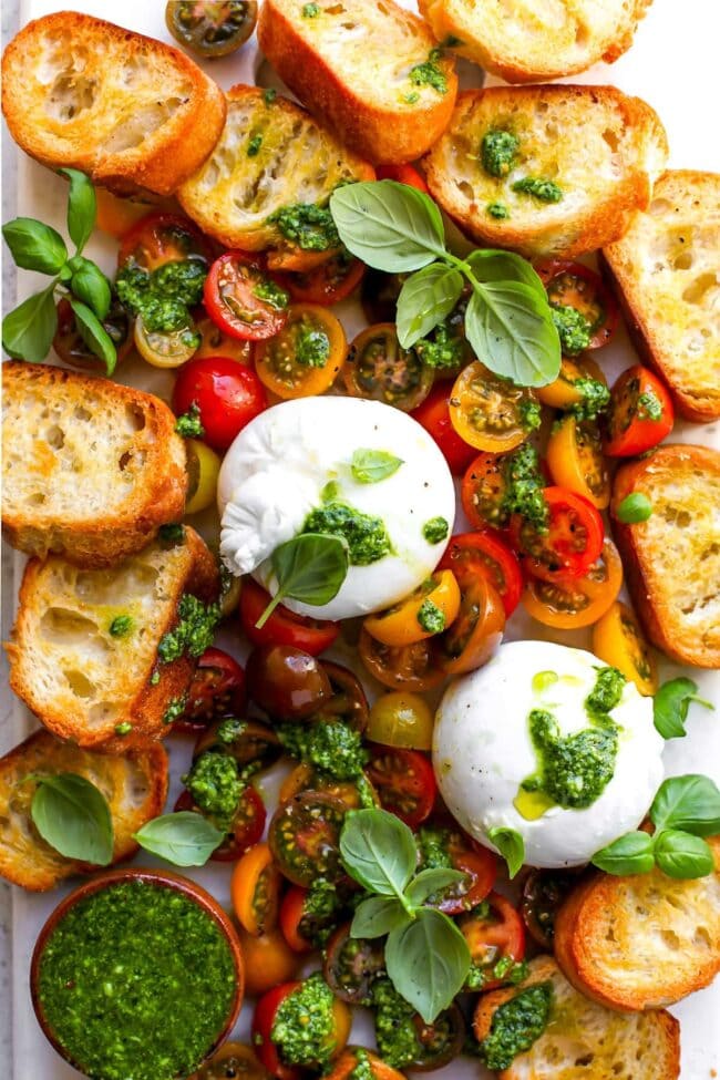 Burrata with tomatoes, pesto, and grilled bread on platter