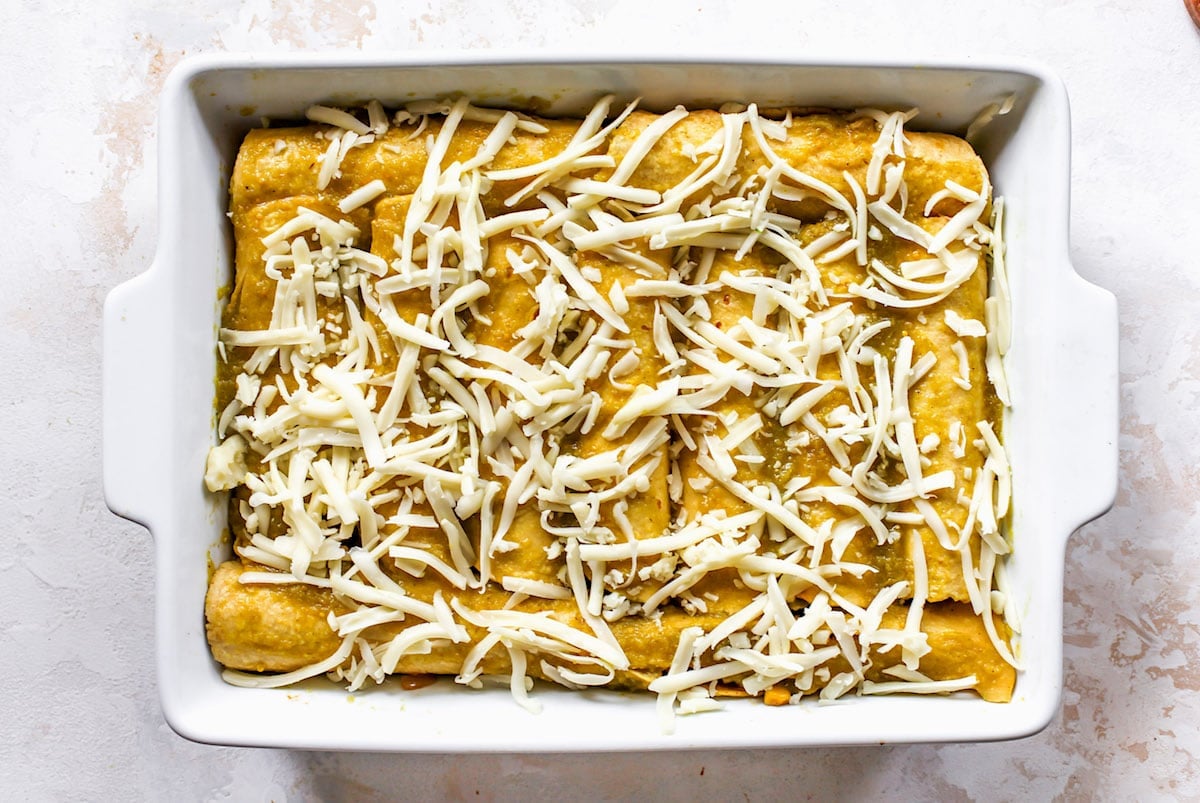 corn and zucchini enchiladas rolled in pan with shredded cheese. 