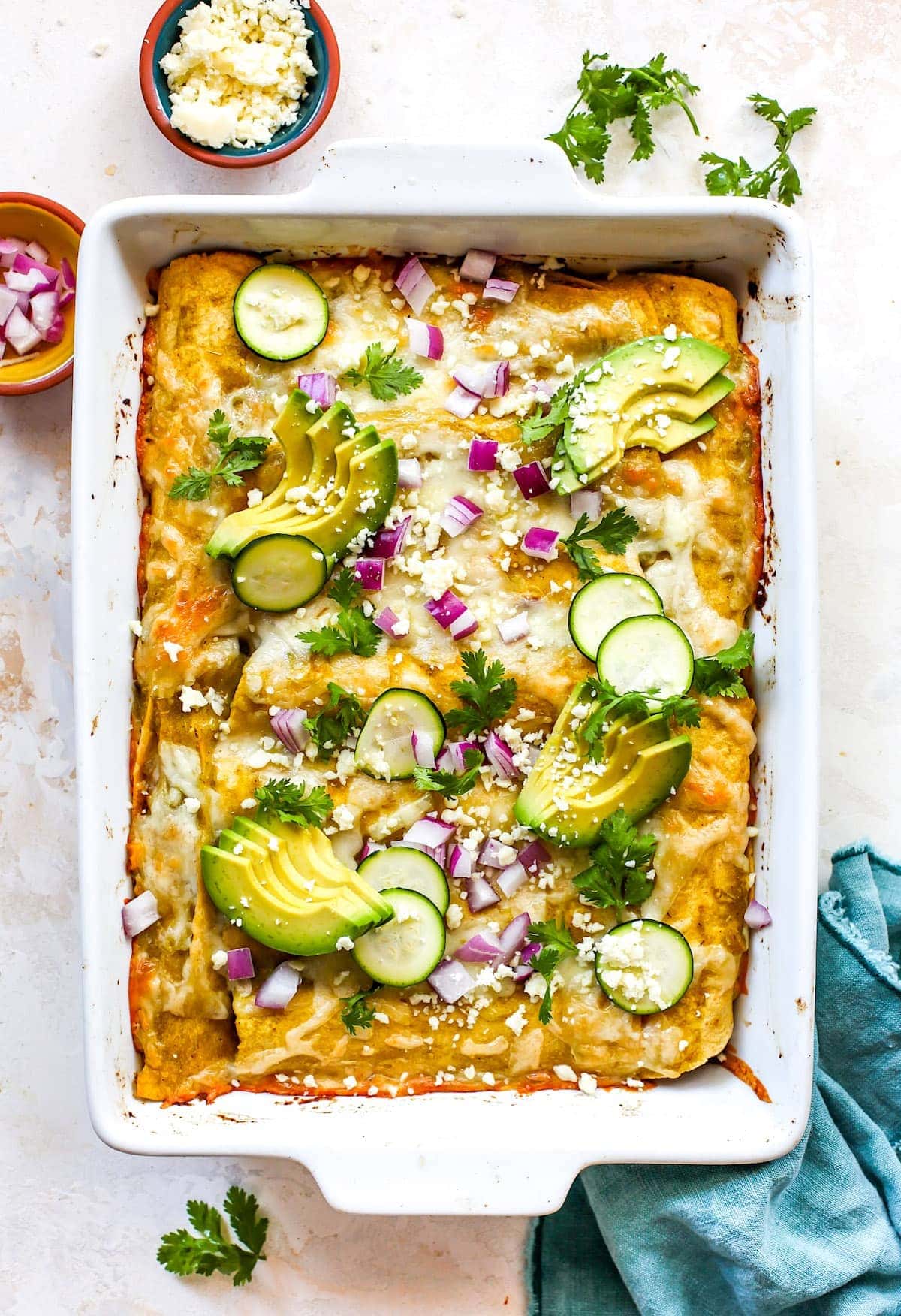 corn and zucchini enchiladas in pan with avocado, cilantro, and red onion. 