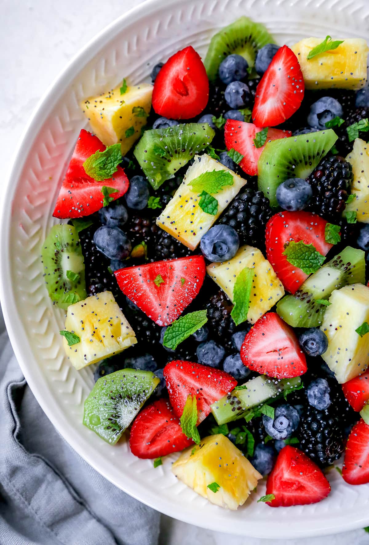close up of fruit salad in bowl with mint and poppyseed dressing.