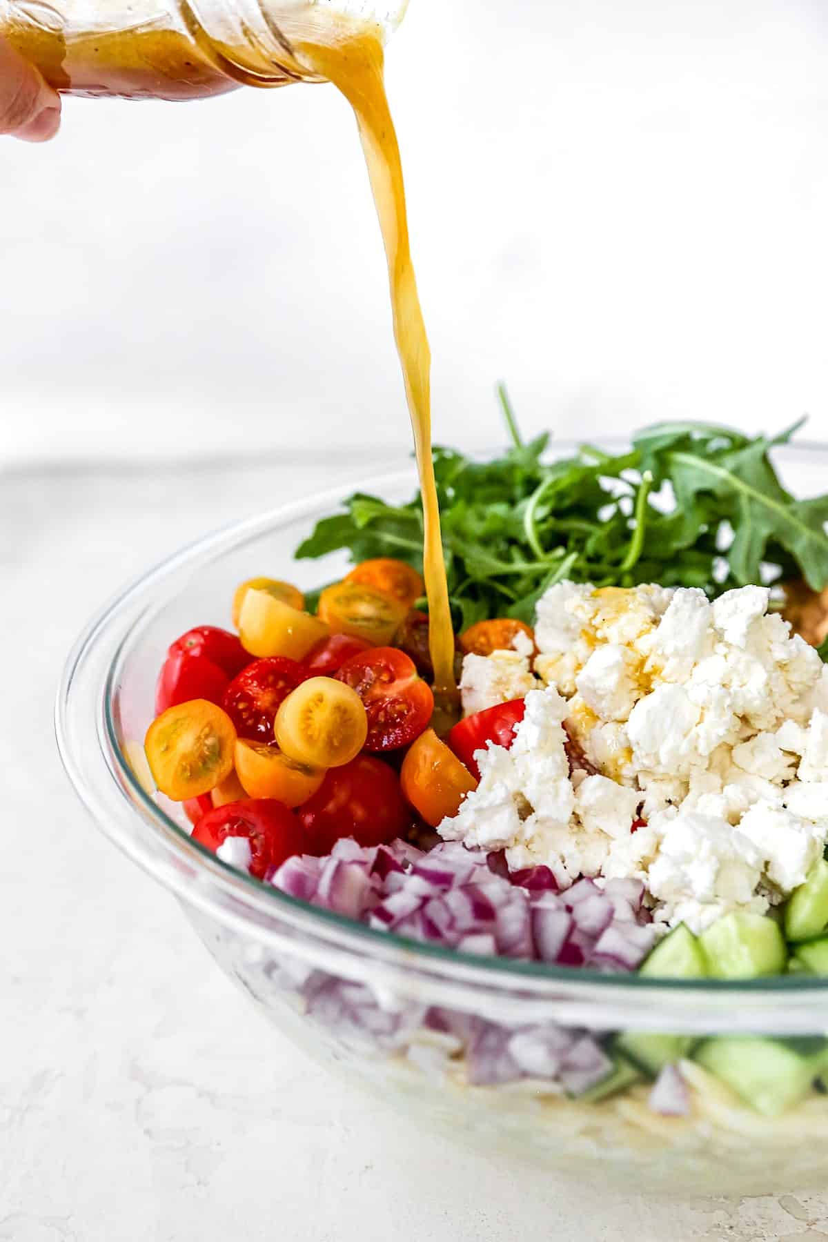 orzo salad in bowl with dressing being drizzled over the salad.