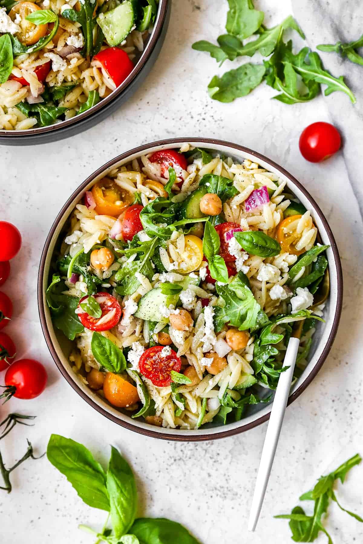 Orzo Salad with arugula, veggies, and feta in bowl with fork.