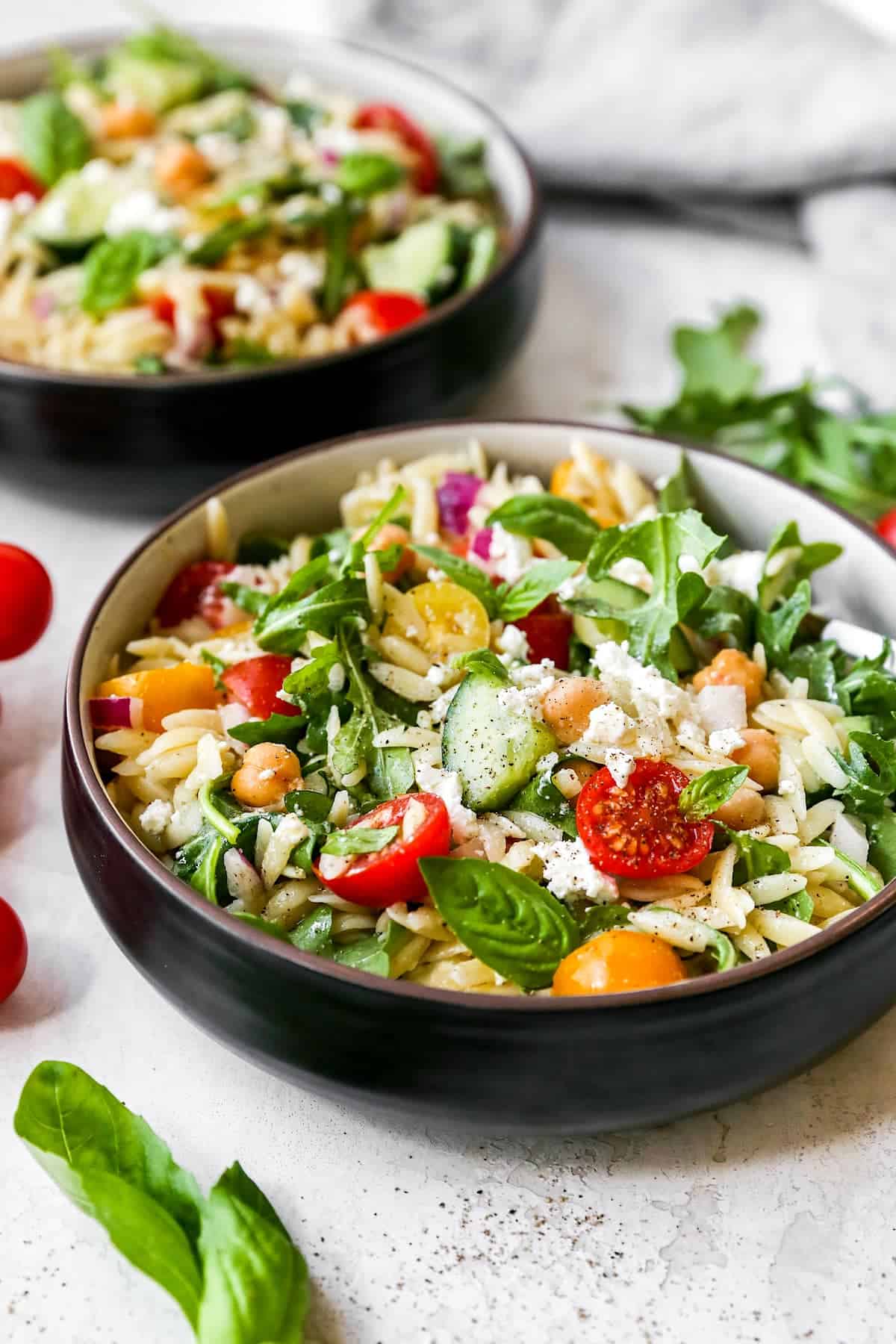 orzo salad with cucumbers, tomatoes, arugula, basil, chickpeas, and feta in bowl. 