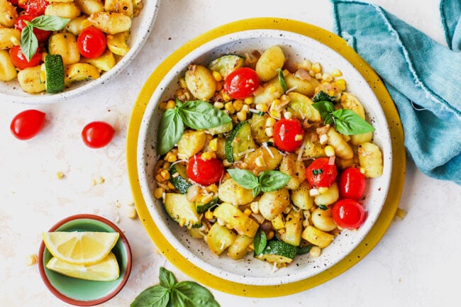 Butter Parmesan Gnocchi with squash, corn, and tomatoes in bowl with basil and lemon wedges