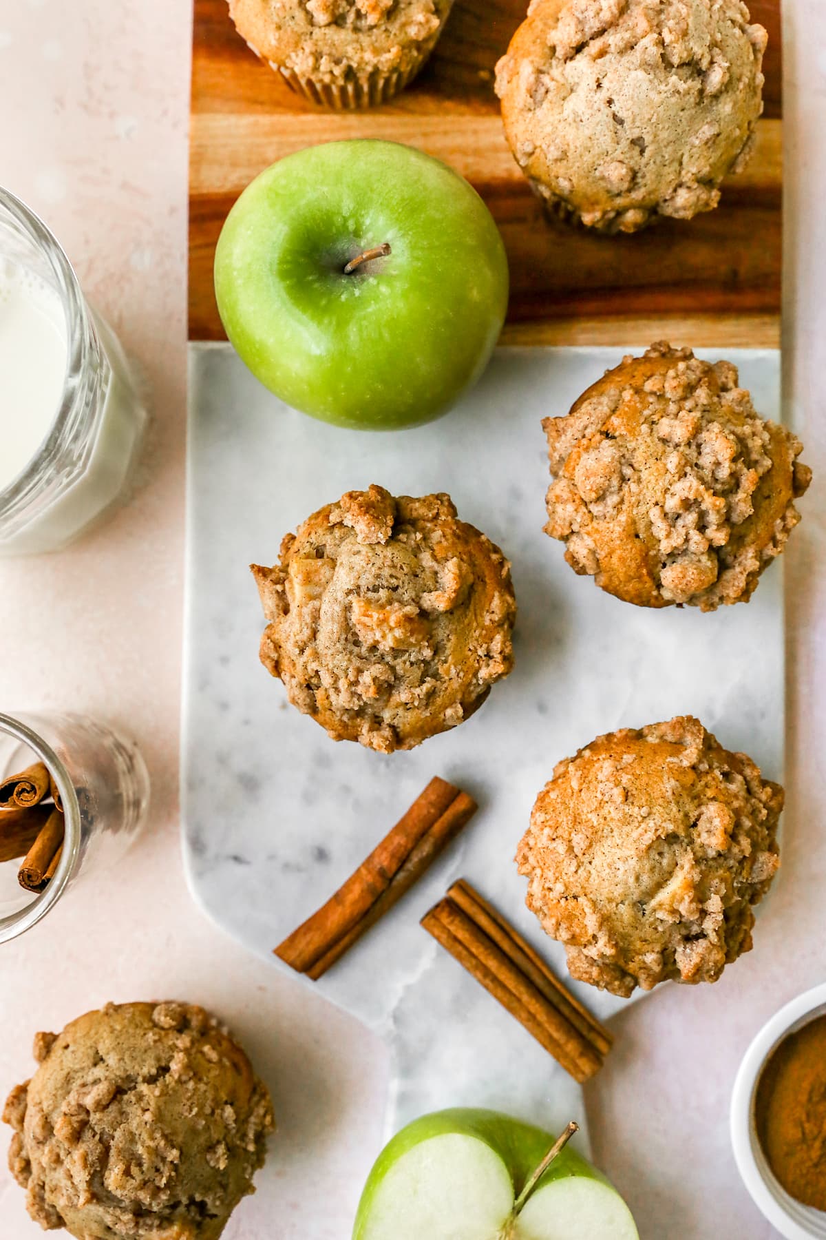 Apple Cinnamon Muffins with crumb topping on board with apples and cinnamon sticks. 