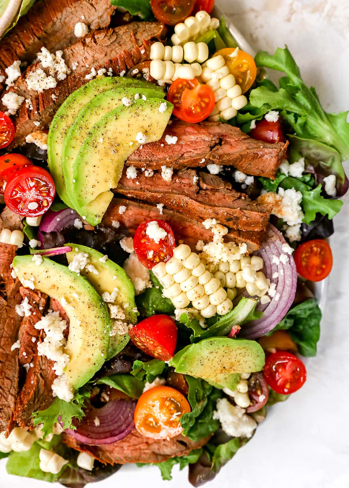 steak salad with avocados, tomatoes, red onion, and corn.