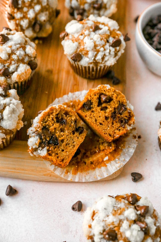 Pumpkin chocolate chip muffin cut in half in paper wrapper on wood board.