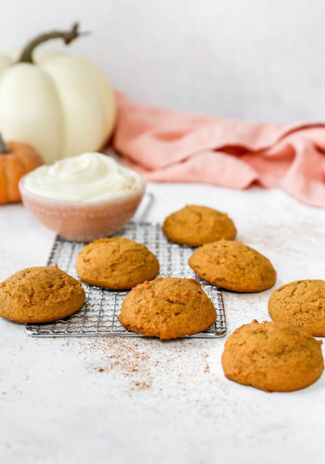 Pumpkin cookies on cooling rack with a bowl of cream cheese frosting.