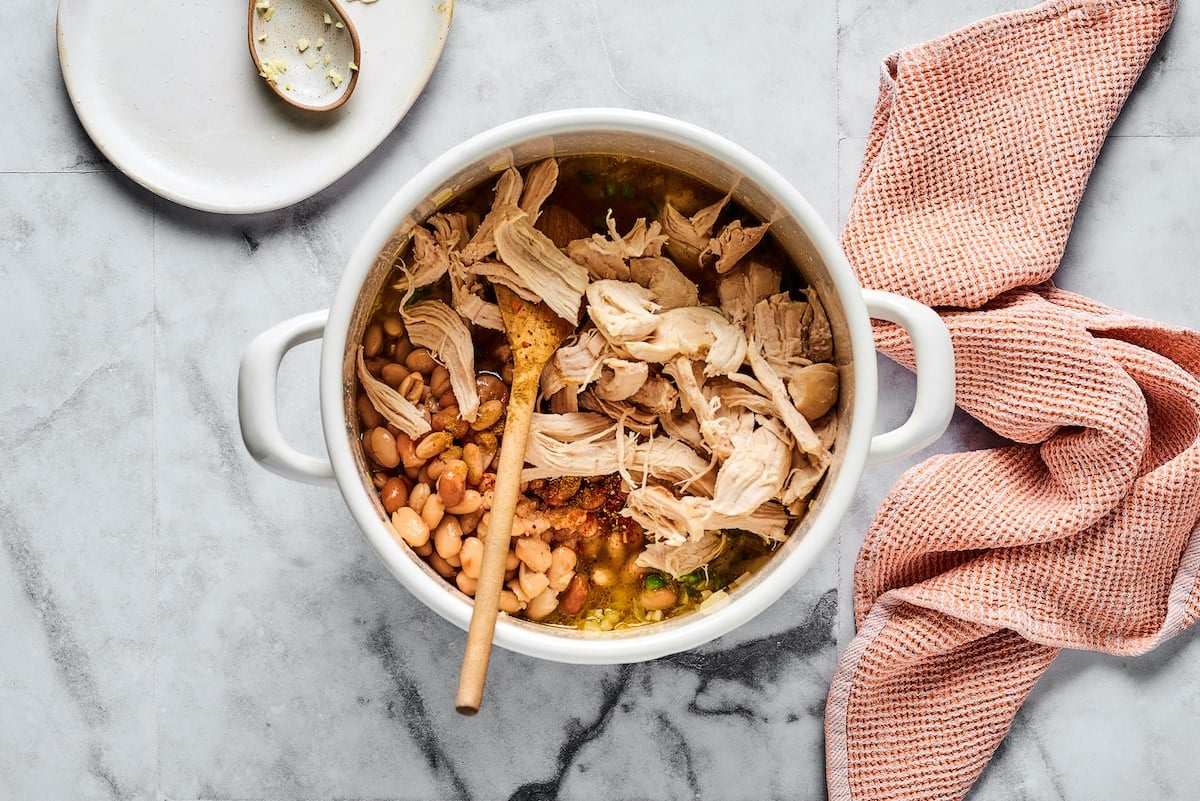 Shredded chicken and white beans added into a large pot with sautéed garlic, onions, and jalapeños.