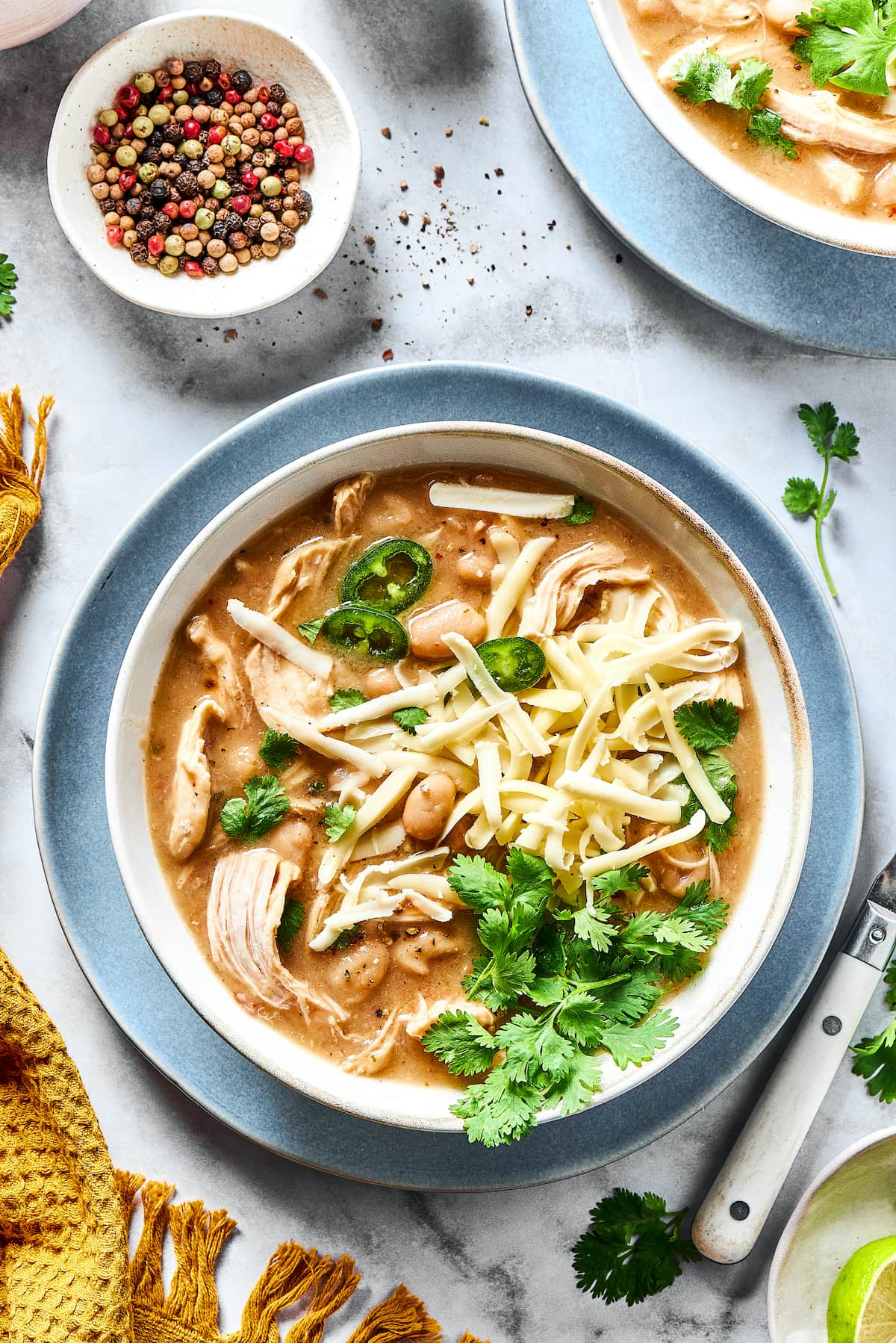 Overhead view of a bowl of white chicken chili garnished with fresh cilantro, next to a small bowl of rainbow peppercorns.