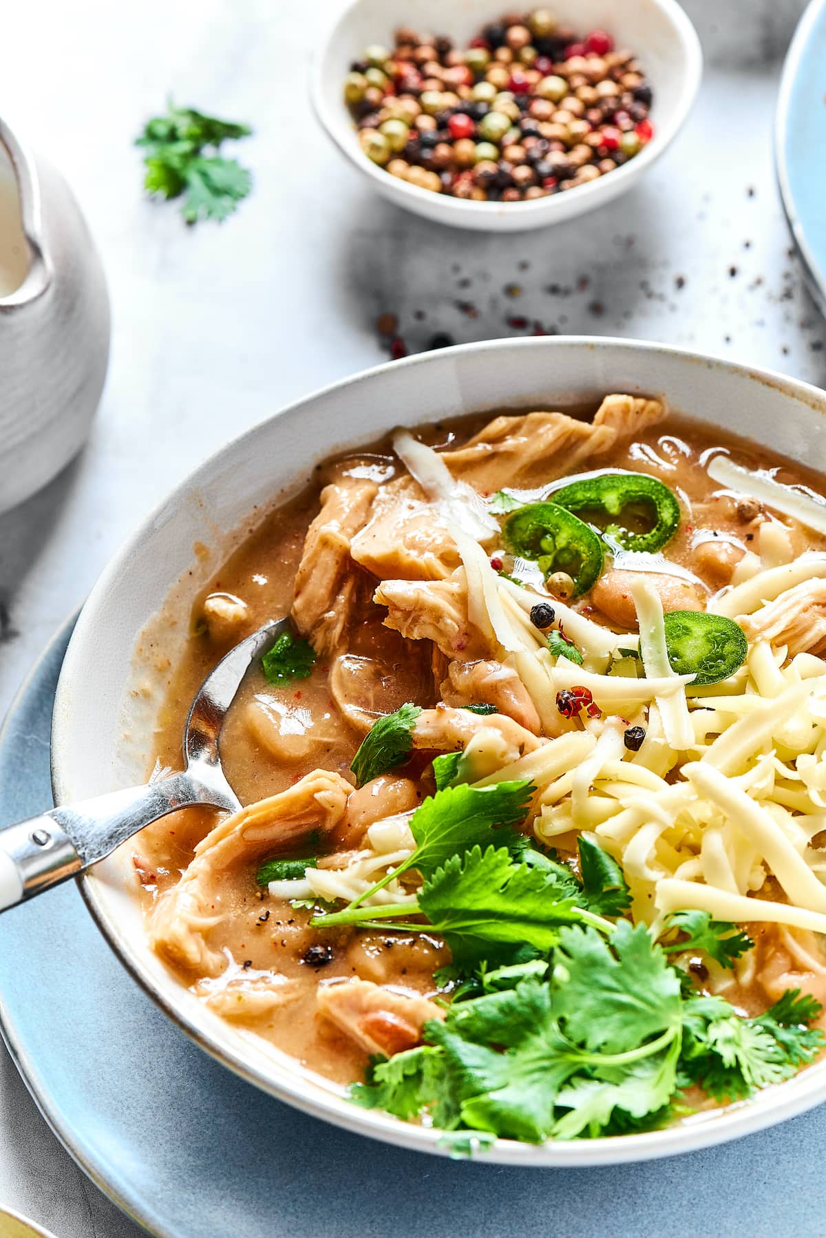 A spoon stuck into a bowl of white chicken chili garnished with fresh cilantro.