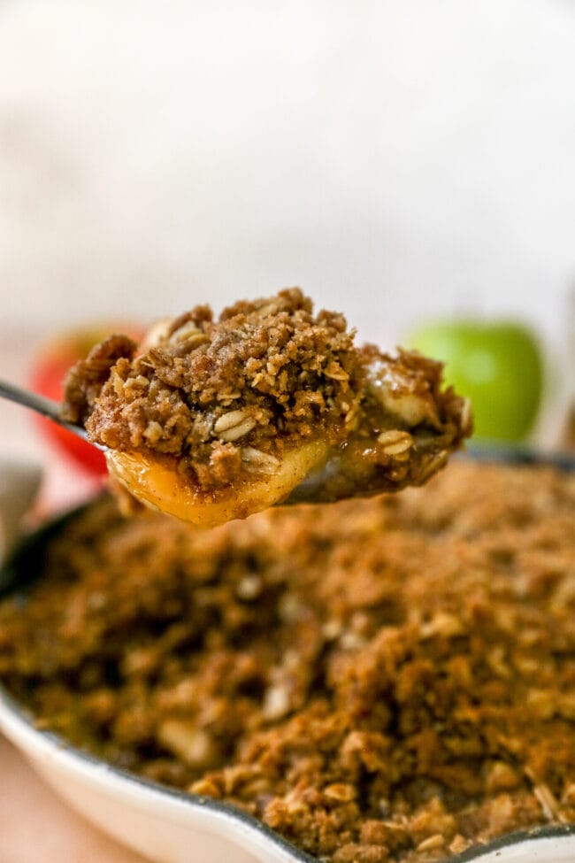 apple crumble in skillet with a spoonful of crumble being lifted out of the skillet. 
