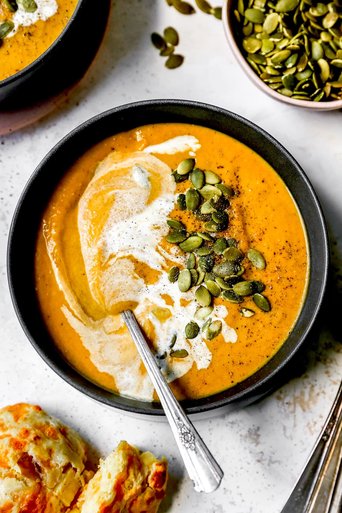 pumpkin soup in bowl with heavy cream, pepitas, and spoon. 