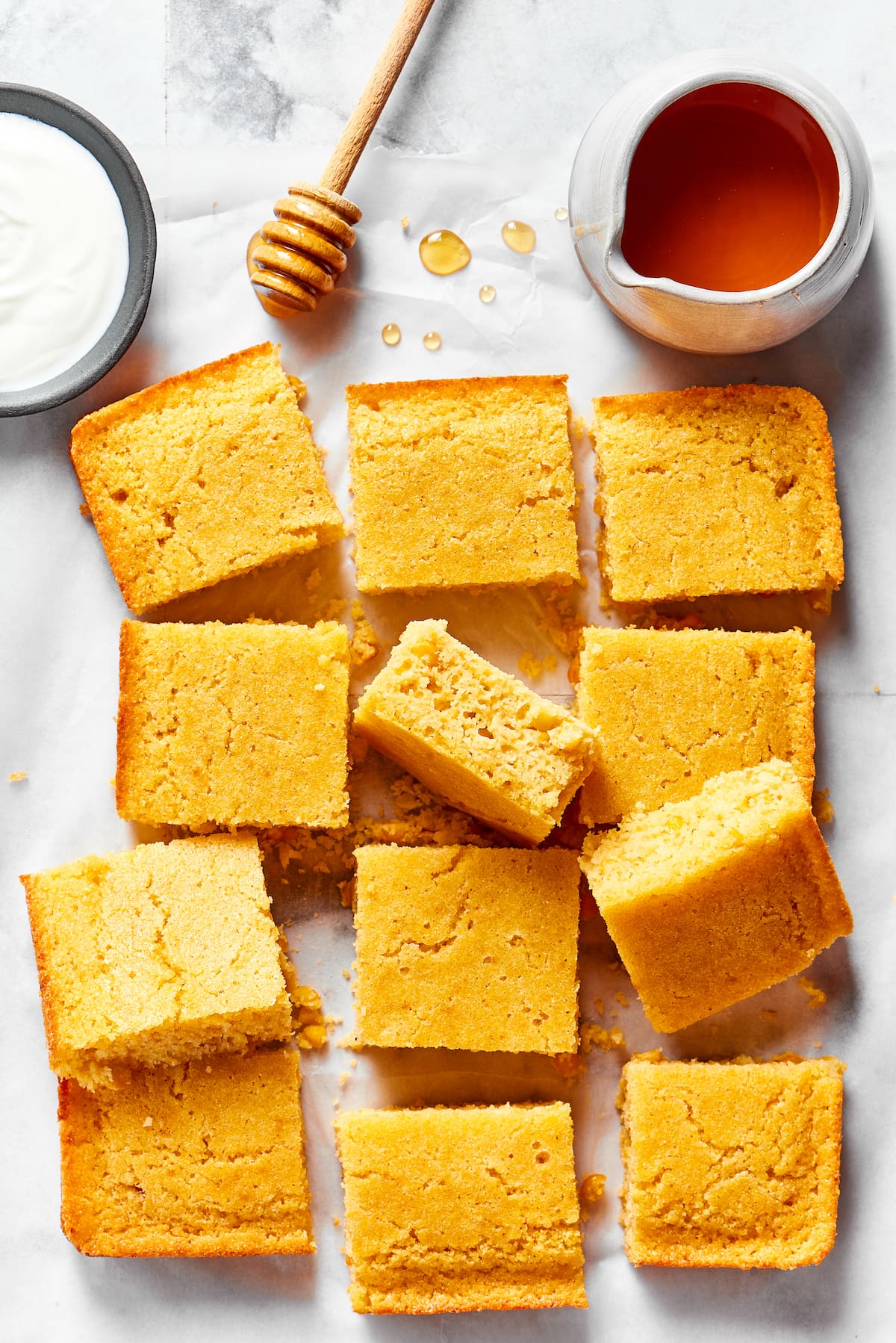 Slices of cornbread on a counter, next to a bowl of honey, a honey stirrer, and a bowl of creme fraiche