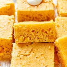 A pile of earny cornbread squares, with creme fraiche and honey on top of the top piece
