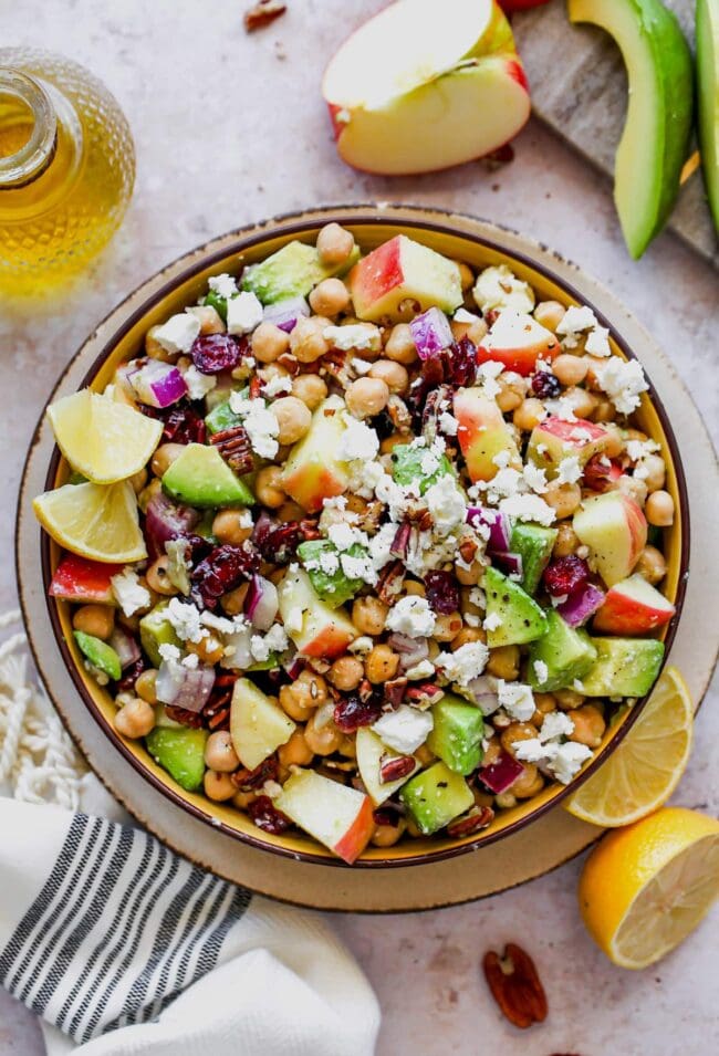 fall chickpea salad in bowl with apples, avocado, dried cranberries, pecans, and goat cheese