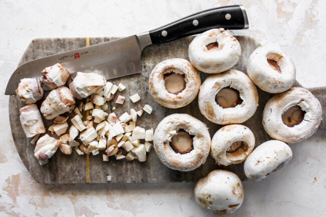 white mushrooms on cutting board with knife.