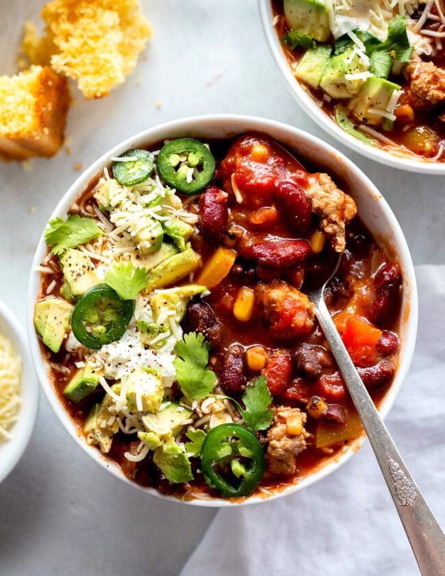turkey chili in bowl with toppings and a spoon. 