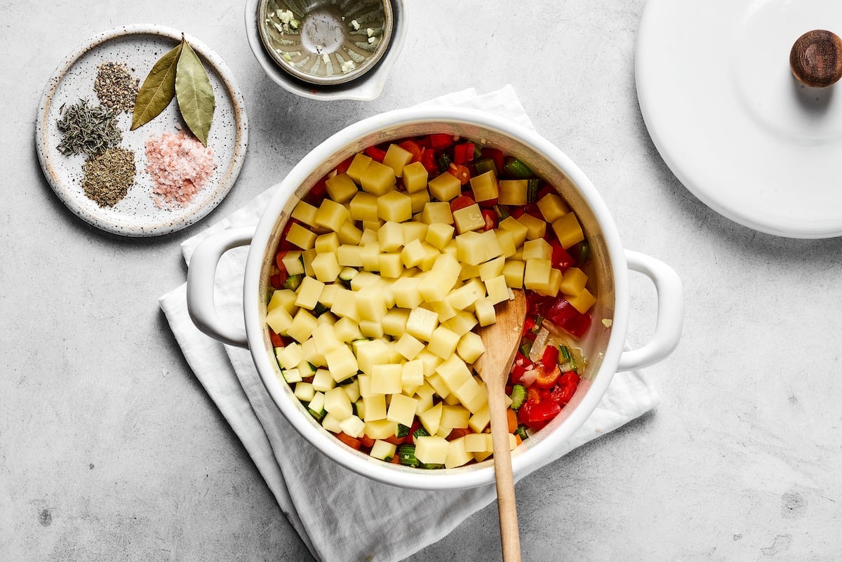 Chopped potatoes are added into the sautéed veggies in a saucepan.