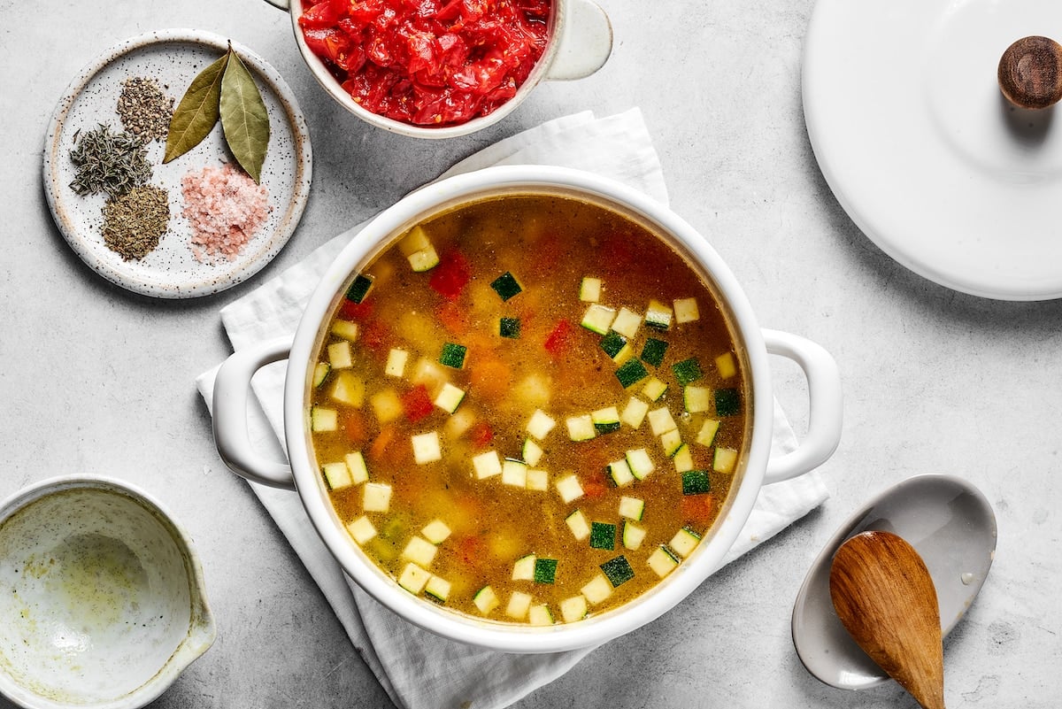 Broth is added to a saucepan with sautéed veggies for soup.