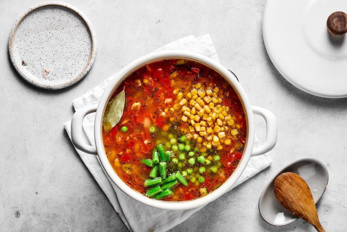 This comforting homemade vegetable soup recipe is a family favorite that's so much better than canned soup! Enjoy a bowl for lunch or dinner. Frozen veggies are added to vegetable soup in a saucepan.
