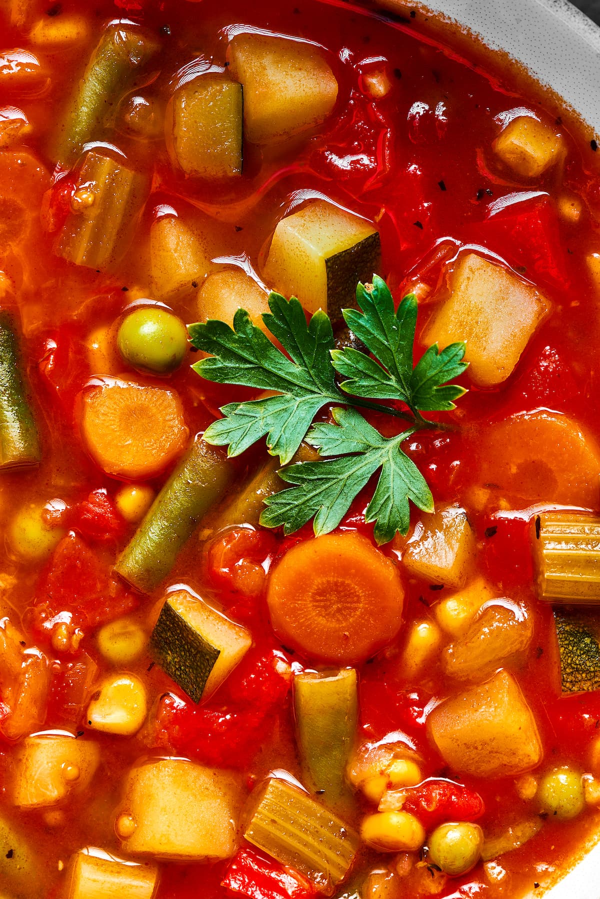 Close up of homemade vegetable soup garnished with a green parsley leaf.