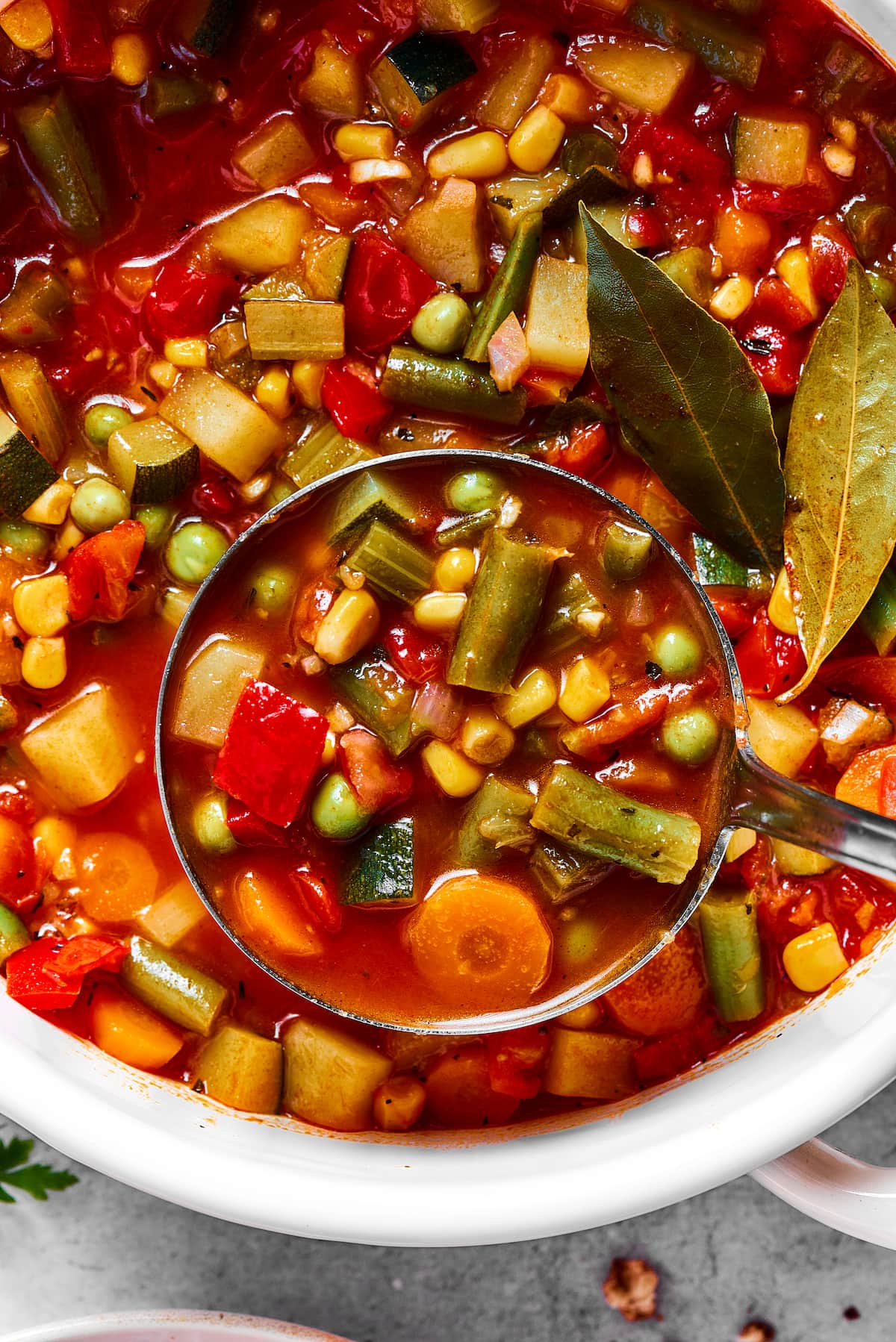 A bowl of homemade vegetable soup with a spoon, next to a large pot. Close up of vegetable soup being ladled from a pot.