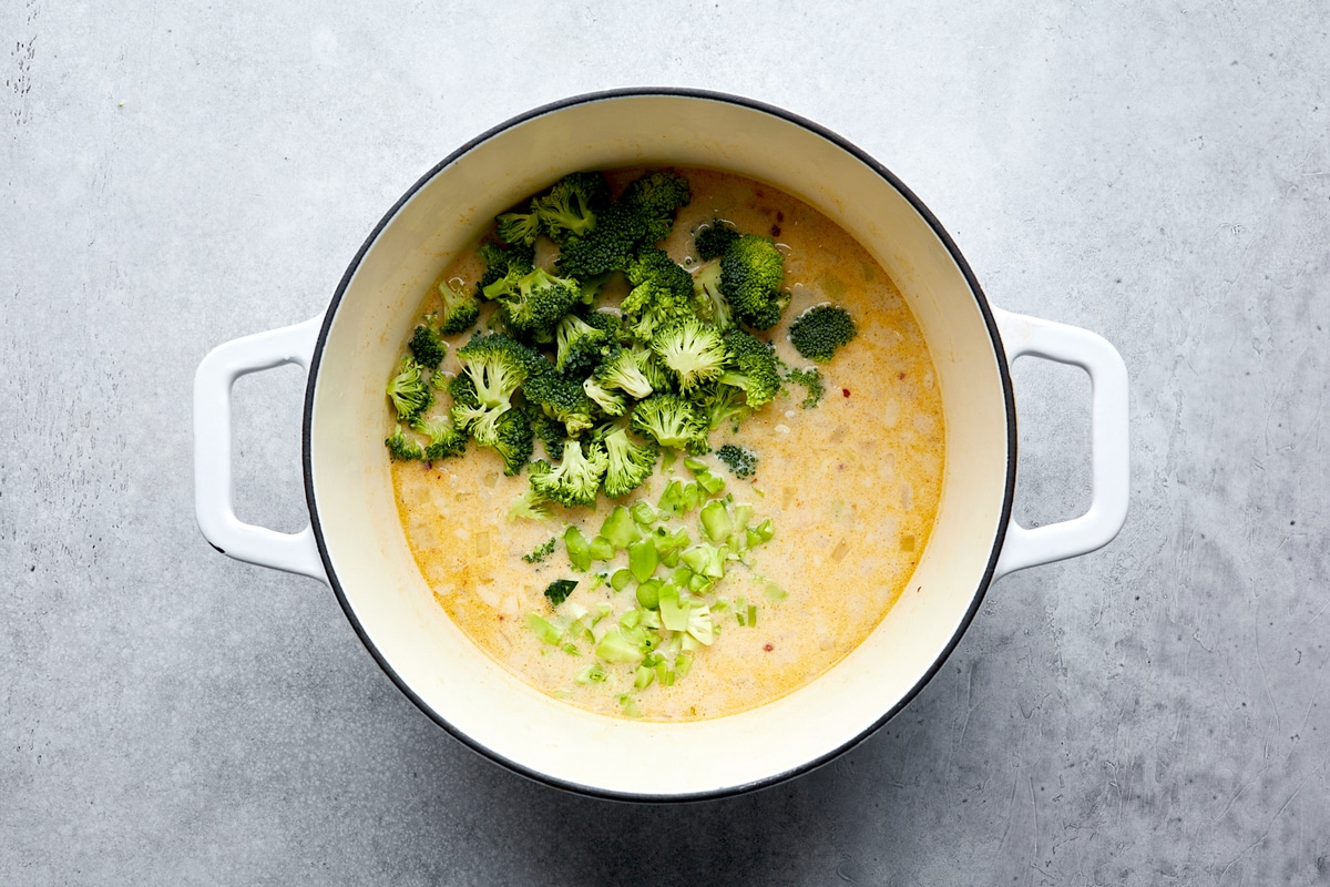 broccoli being added to broccoli cheese soup in pot. 