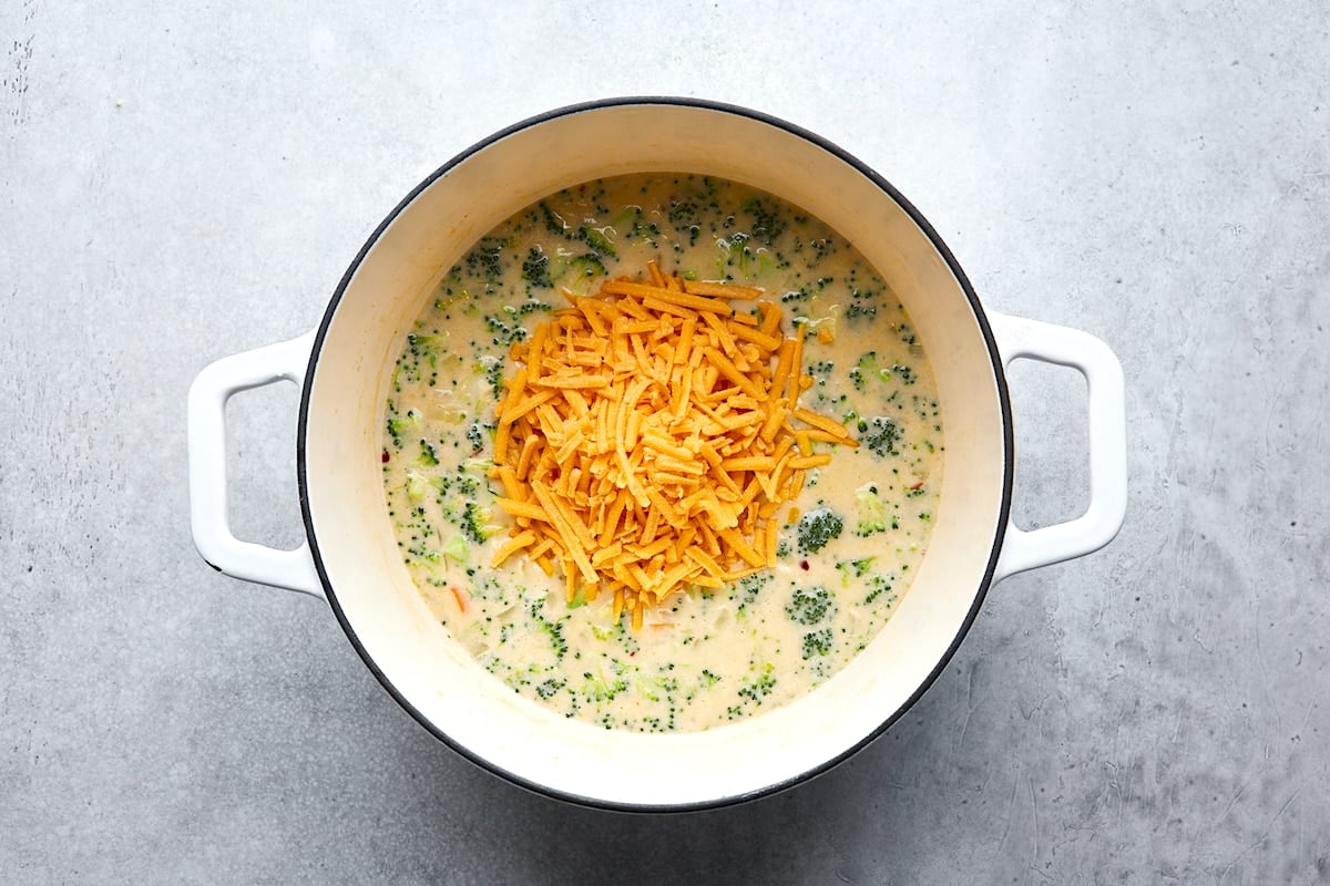 shredded cheese being added to broccoli cheese soup in pot. 