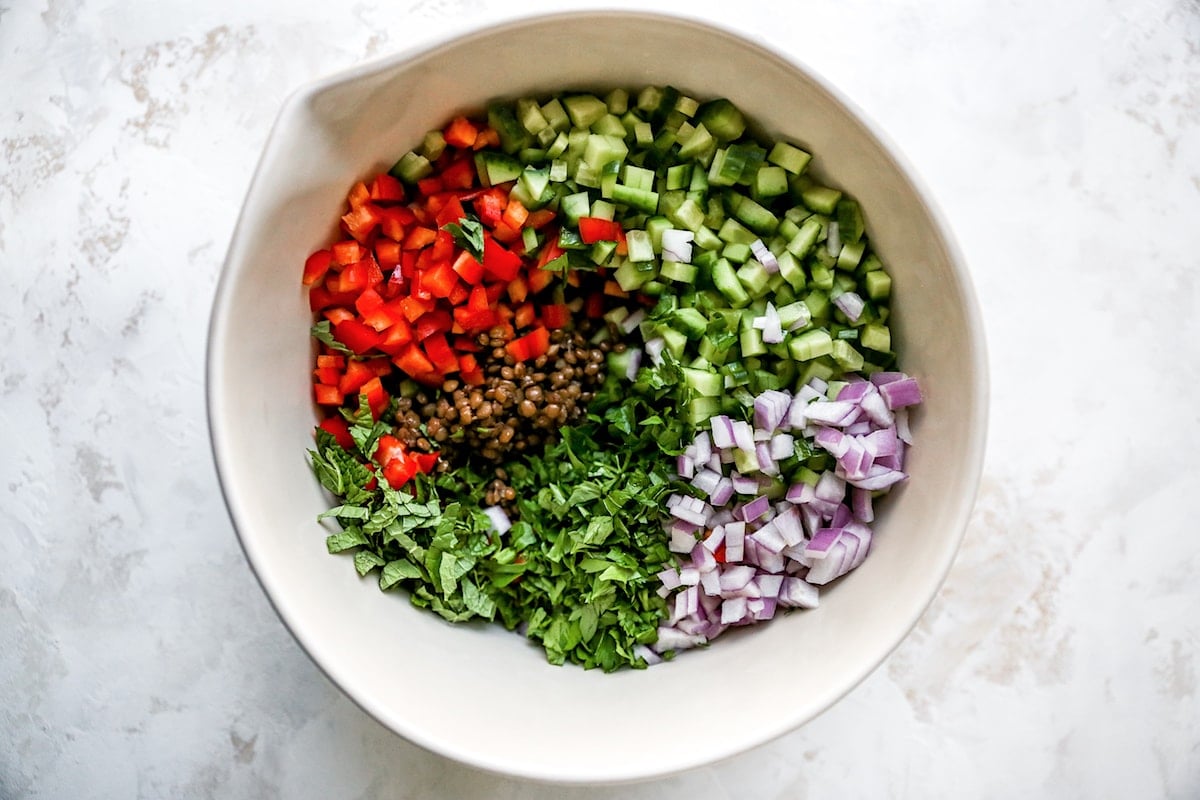 lentils, red pepper, cucumber, red onion, and herbs in bowl to make lentil salad. 