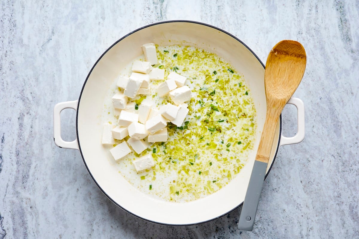 cream cheese, garlic, onion, jalapeño, and oil in skillet with wooden spoon. 