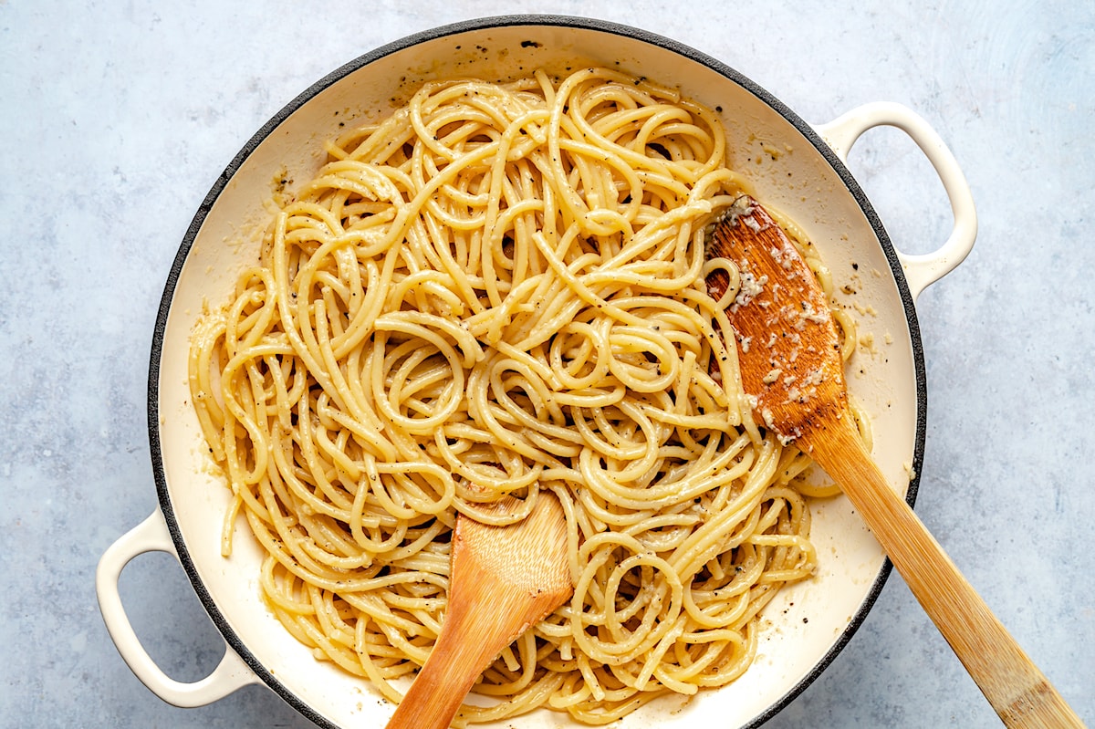 cacio e pepe in skillet with cheese and wooden serving spoons. 