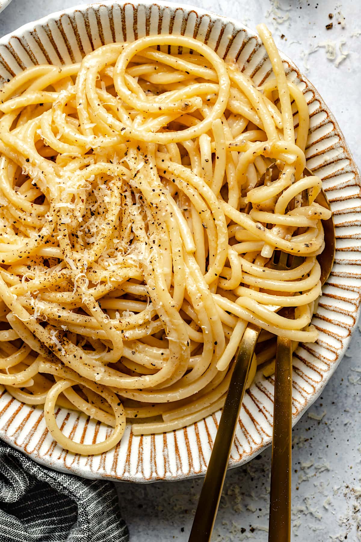 bucatini cacio e pepe pasta in bowl with freshly grated Parmessan cheese.