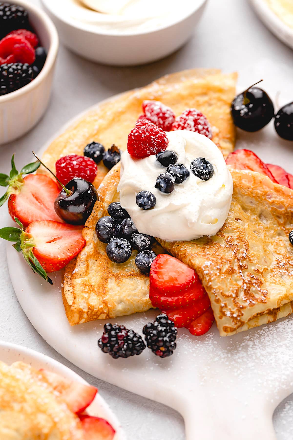 crepes on plate with whipped cream, berries, and powdered sugar.