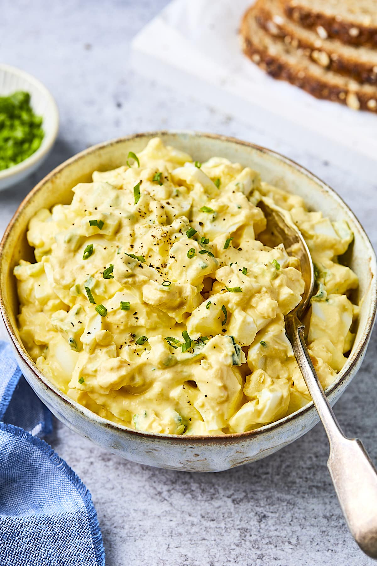 egg salad in bowl with chives and a spoon. 