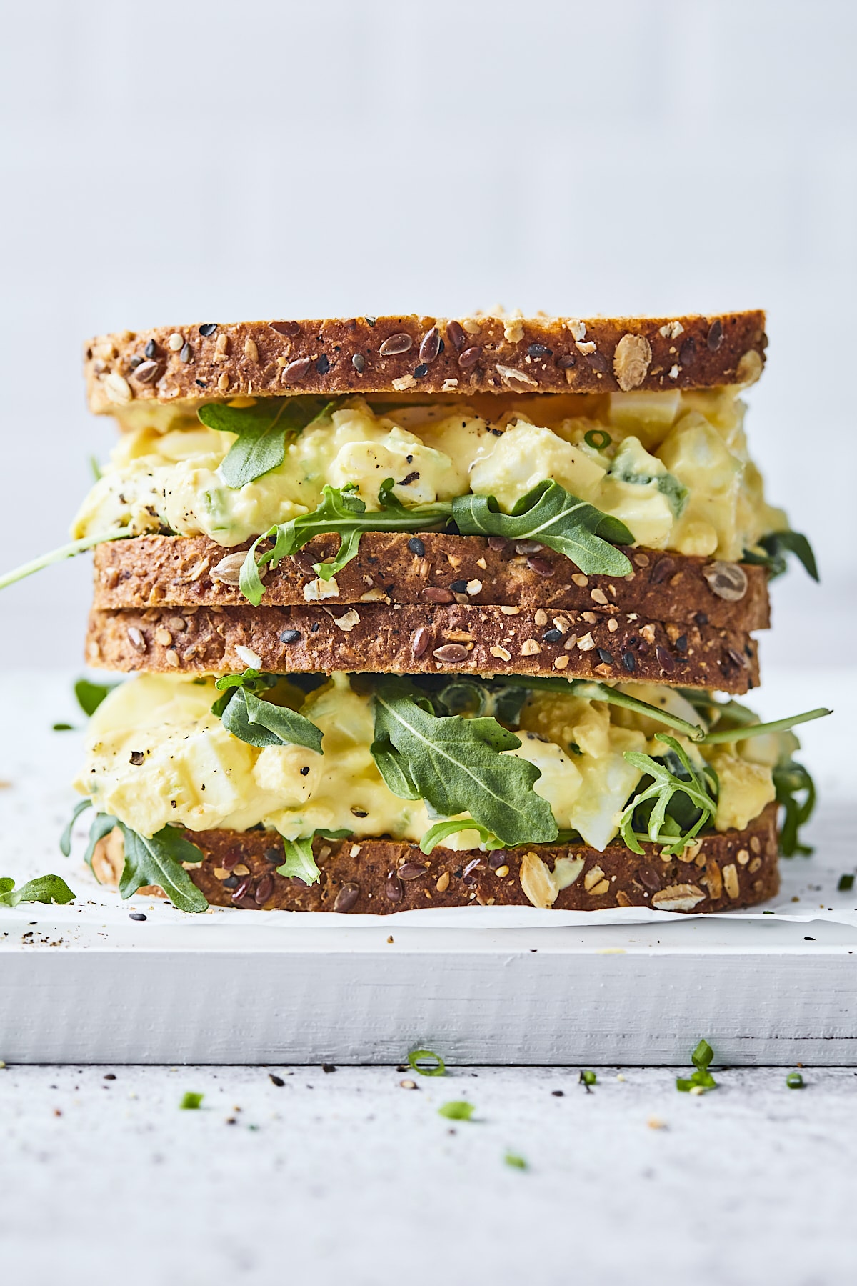2 Egg salad sandwiches stacked on top of each other with arugula on wheat bread.