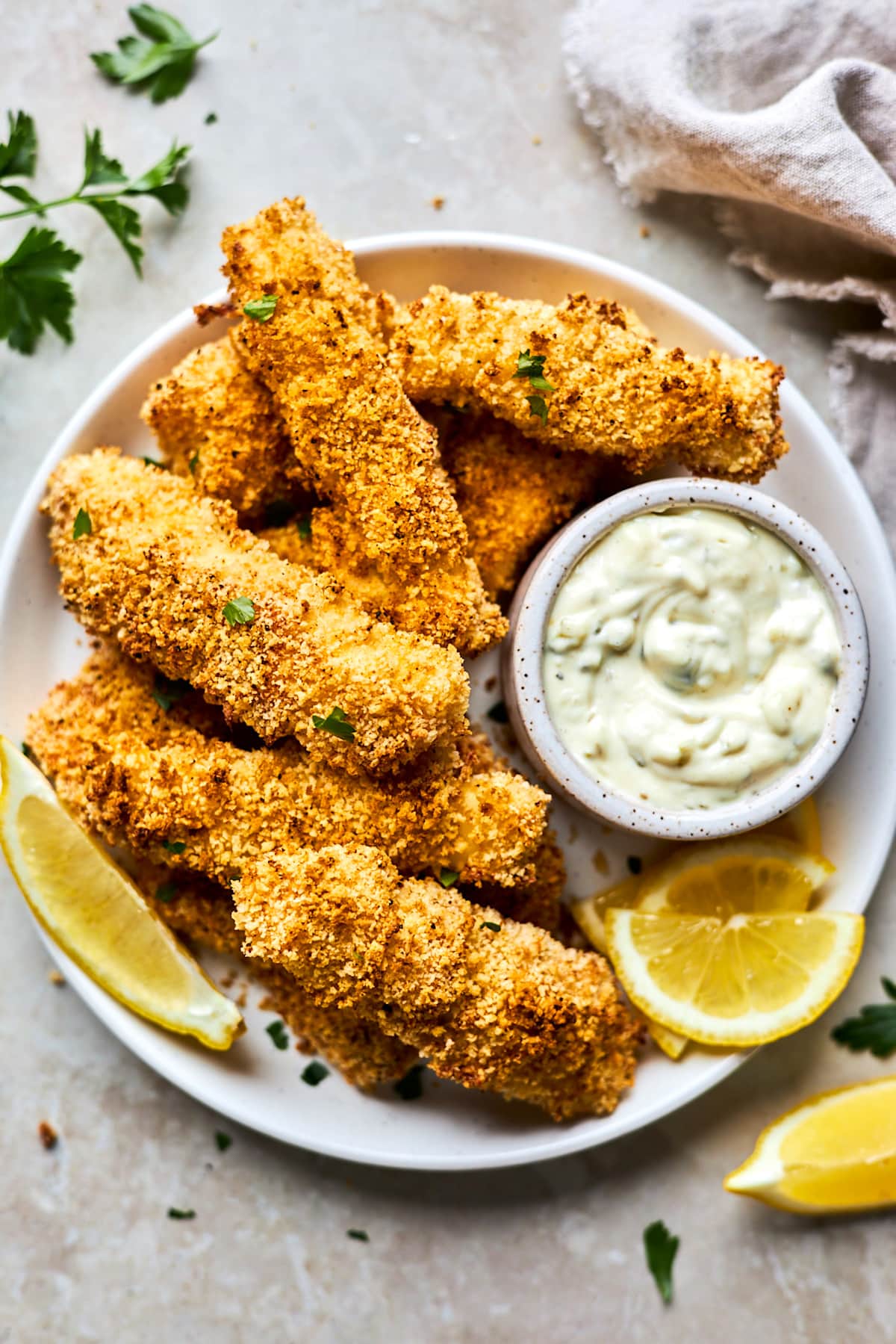 crispy homemade fish sticks on plate with small bowl of tartar sauce and lemons. 