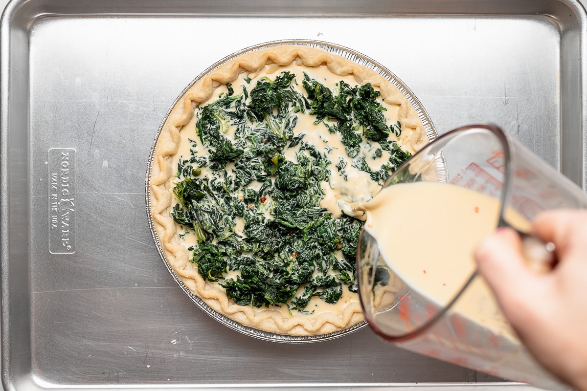 egg mixture being poured into unbaked spinach quiche. 
